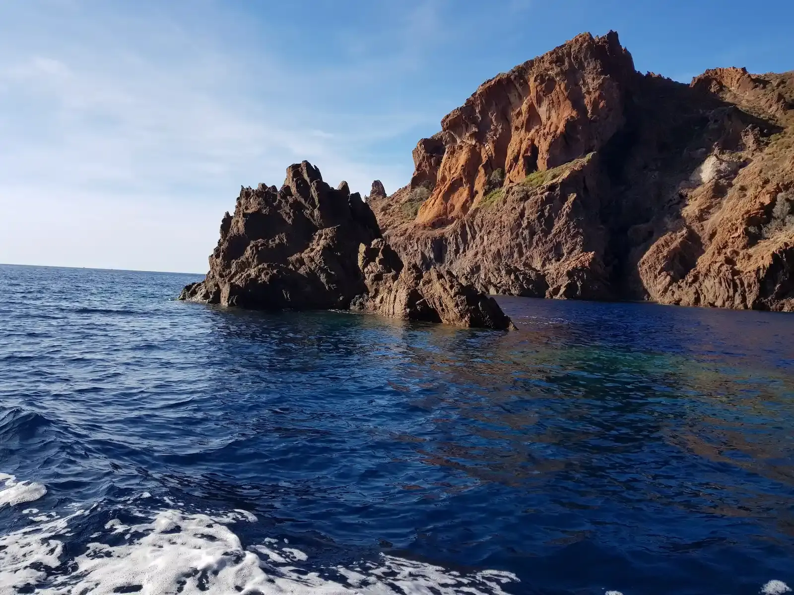 Rochers déchiquetés émergeant d'une mer bleu foncé sous un soleil voilé en Corse.
