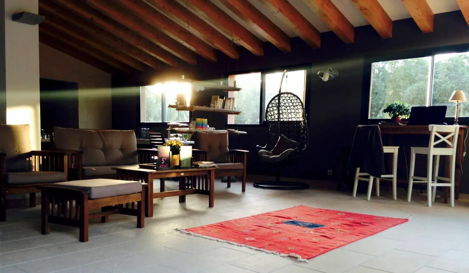 Intérieur spacieux et chaleureux d'une salle commune ou salon de détente au Camping Milella à Propriano, avec poutres apparentes, canapés en bois et un fauteuil suspendu.