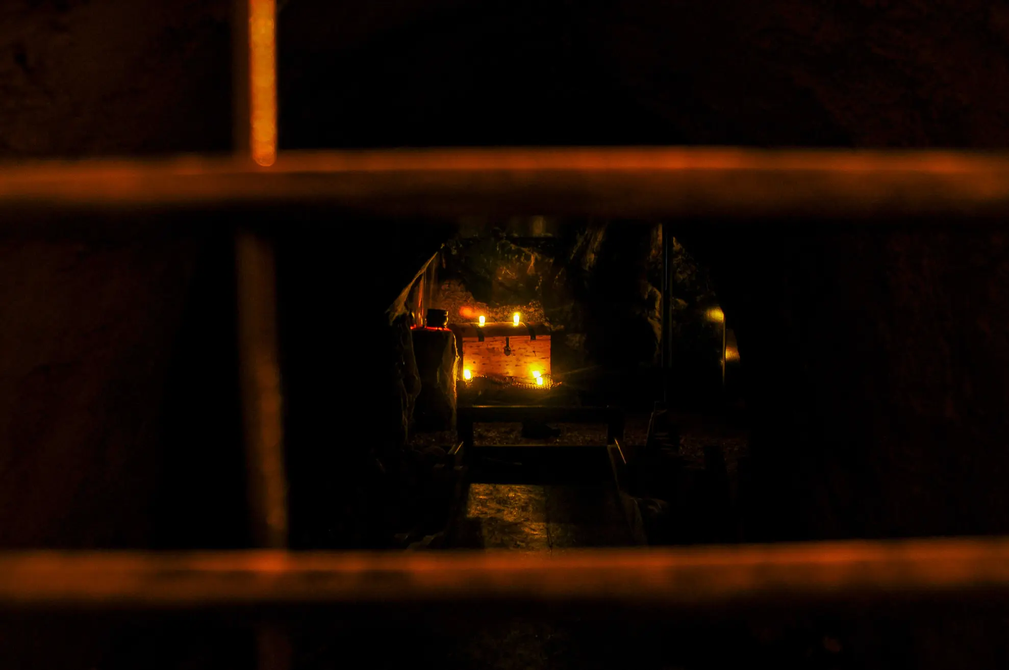 Vue à travers des barreaux d'un coffre au trésor éclairé par des bougies dans une alcôve sombre.