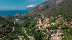 ue aérienne par drone du village de Porto et de son golfe en Corse-du-Sud. Le village aux toits rouges est niché dans une vallée verdoyante au pied de montagnes couvertes de maquis. La rivière Porto serpente vers la mer Méditerranée, où l'on distingue la tour génoise et la marina avec de nombreux bateaux de plaisance amarrés. Le Camping Les Oliviers est situé sur les hauteurs du village.