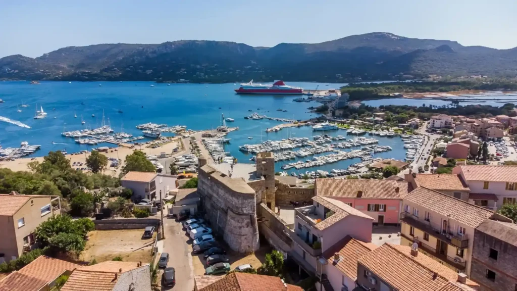 citadelle-de-porto-vecchio-en-corse Vue aérienne du port de plaisance de Porto-Vecchio avec ses bateaux amarrés, ses toits en tuiles et la citadelle historique en arrière-plan.
