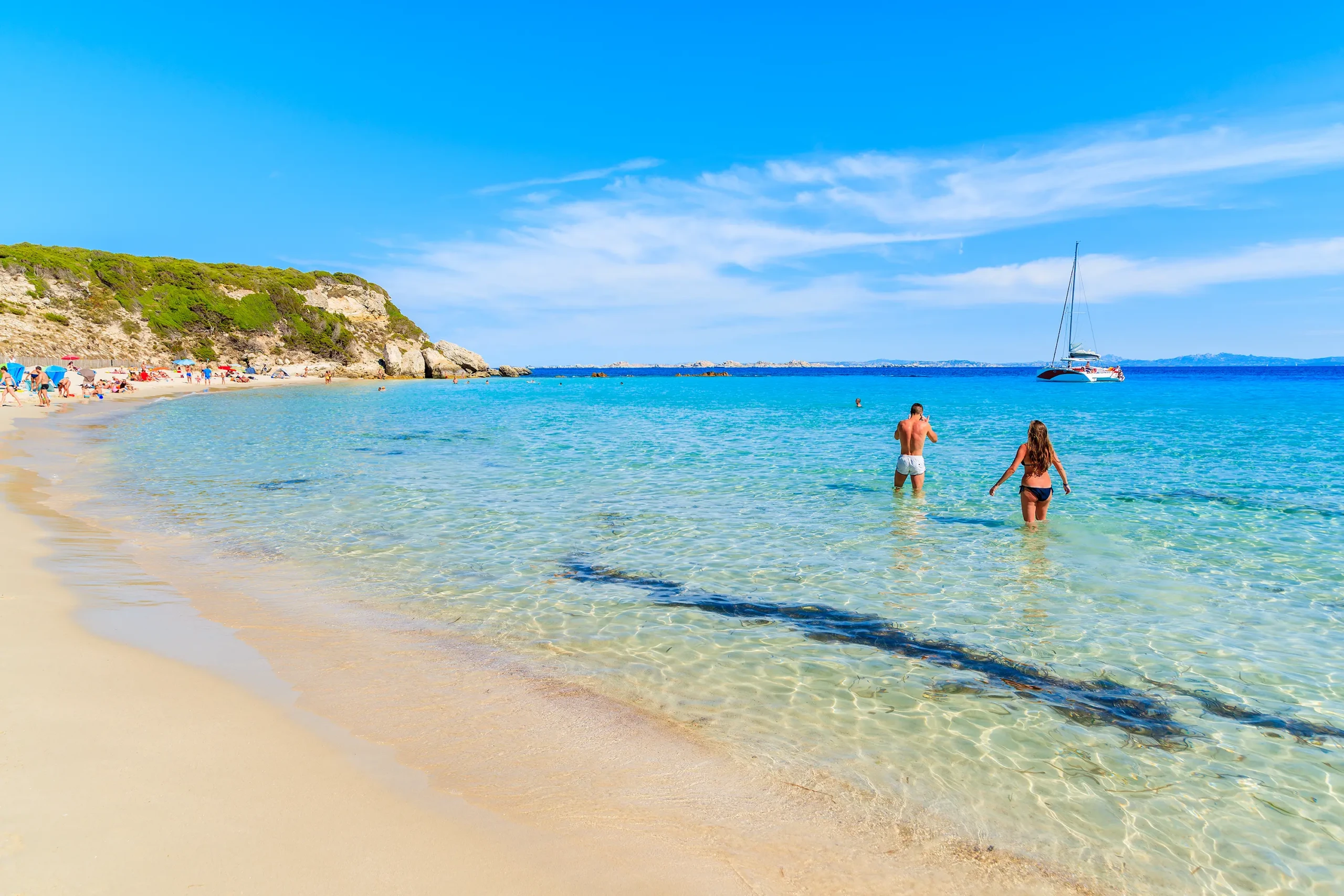 Un homme et une femme en maillot de bain marchant dans l'eau limpide et transparente de la plage du Grand Sperone à Bonifacio.